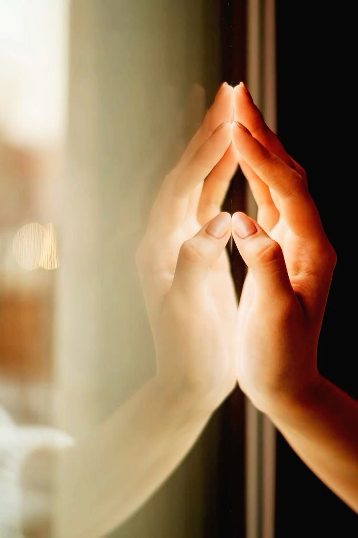 Divas rokas pieliktas pie loga stikla siltā saules gaismā